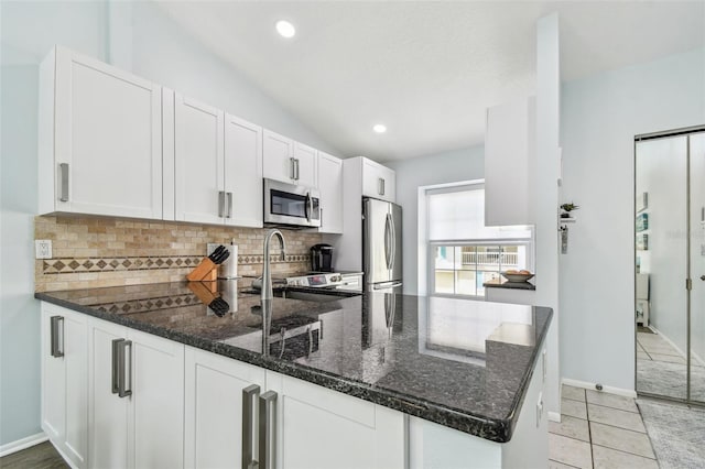 kitchen featuring kitchen peninsula, dark stone counters, white cabinets, and appliances with stainless steel finishes