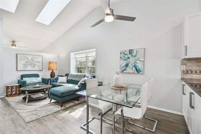 dining space with wood-type flooring, high vaulted ceiling, ceiling fan, and a skylight