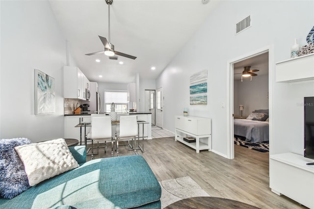 living room featuring light hardwood / wood-style flooring, high vaulted ceiling, and ceiling fan