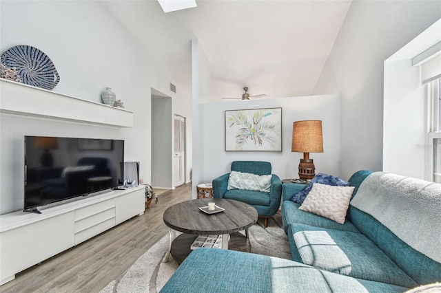 living room with ceiling fan, high vaulted ceiling, a skylight, and light hardwood / wood-style floors