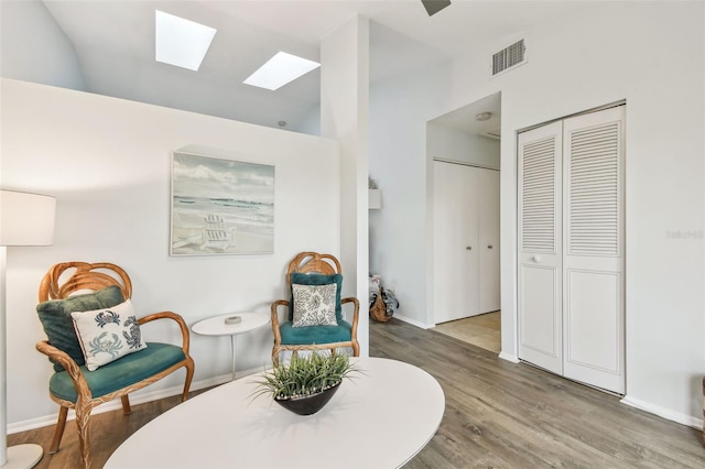 living area with vaulted ceiling with skylight and hardwood / wood-style floors