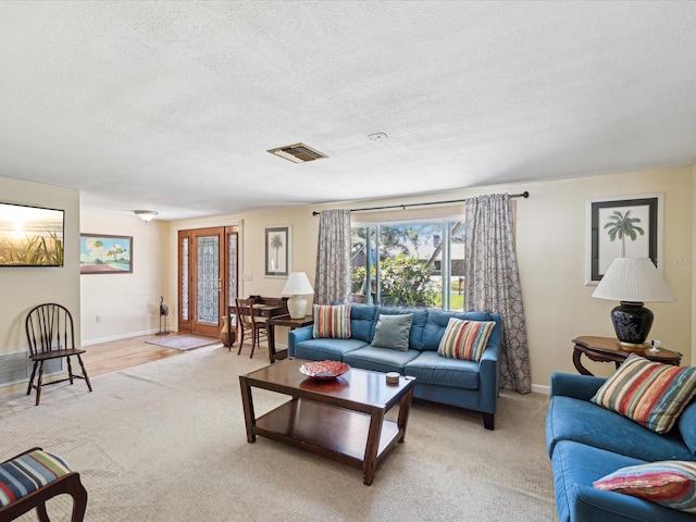 living room featuring baseboards, visible vents, a textured ceiling, and light colored carpet