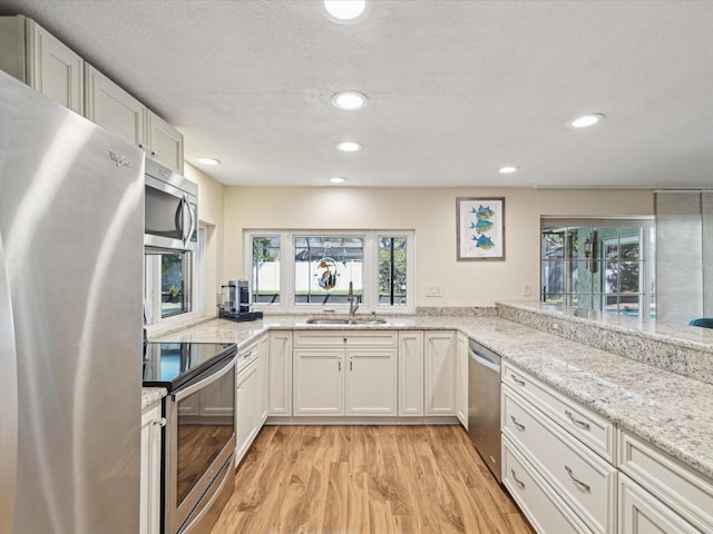 kitchen with stainless steel appliances, recessed lighting, light wood-style flooring, a sink, and light stone countertops