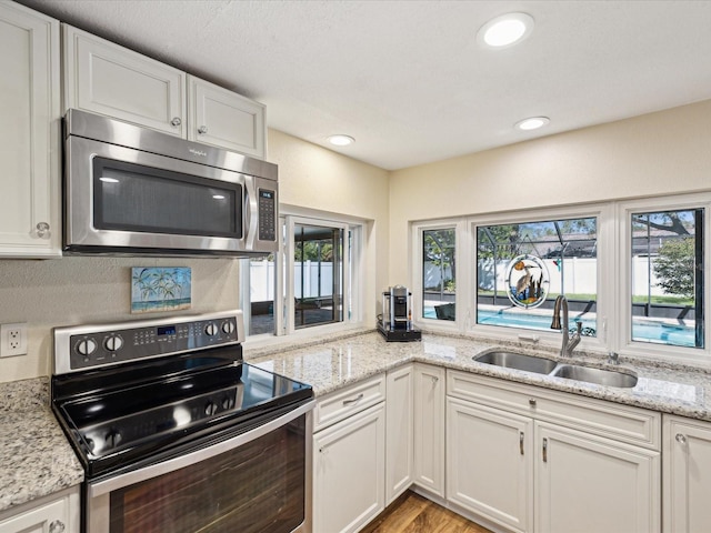 kitchen featuring appliances with stainless steel finishes, a wealth of natural light, white cabinets, and a sink