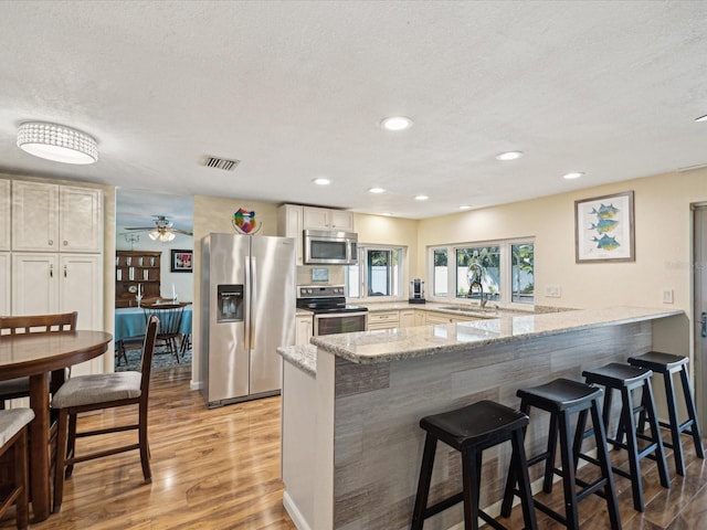 kitchen featuring visible vents, light stone counters, a peninsula, stainless steel appliances, and light wood-type flooring