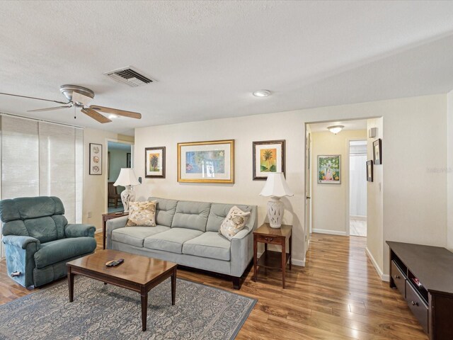 living area featuring visible vents, ceiling fan, a textured ceiling, wood finished floors, and baseboards