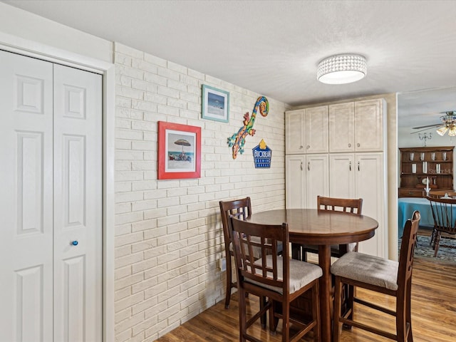 dining room featuring brick wall, dark wood-type flooring, and a ceiling fan