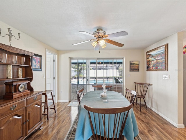 dining room with a ceiling fan, a textured ceiling, baseboards, and wood finished floors