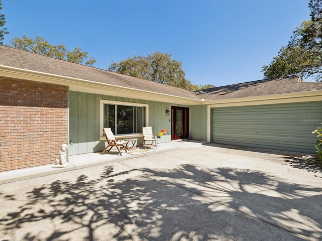 view of exterior entry featuring an attached garage, concrete driveway, and brick siding