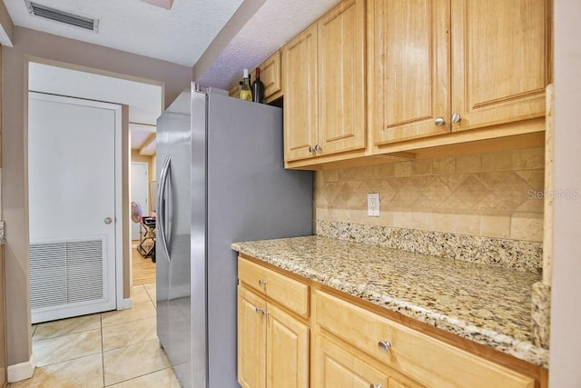 kitchen featuring light tile patterned floors, stainless steel refrigerator, backsplash, light stone countertops, and light brown cabinetry