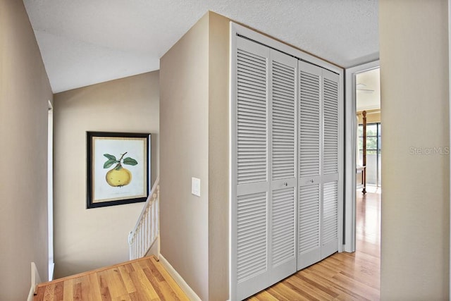 hallway with lofted ceiling, a textured ceiling, and light wood-type flooring