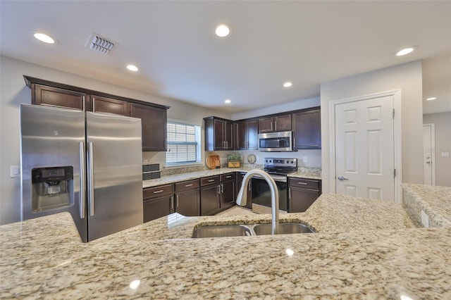 kitchen with sink, dark brown cabinets, stainless steel appliances, and light stone countertops