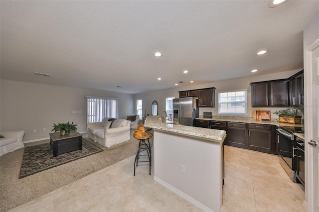 kitchen featuring a breakfast bar, appliances with stainless steel finishes, dark brown cabinets, a center island with sink, and light tile patterned flooring