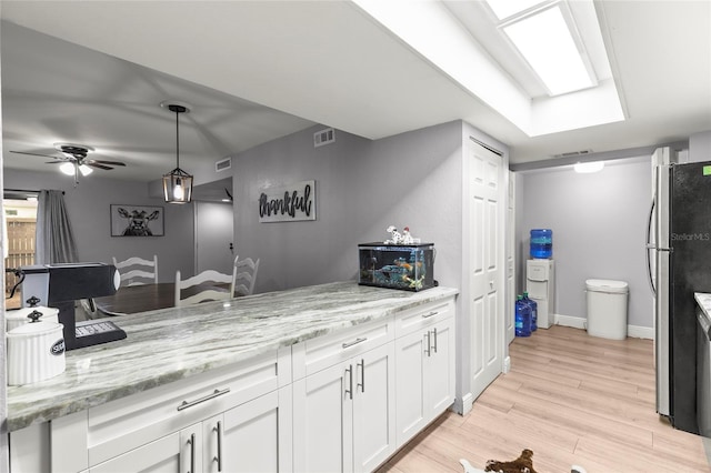 kitchen featuring stainless steel fridge, white cabinetry, light stone countertops, light hardwood / wood-style floors, and decorative light fixtures