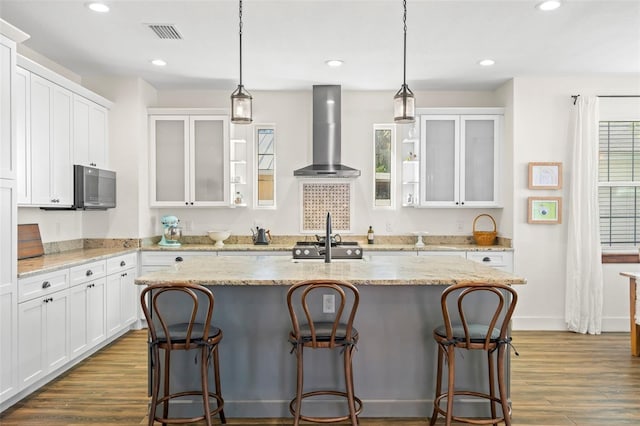 kitchen featuring white cabinetry, wall chimney range hood, a breakfast bar area, and an island with sink