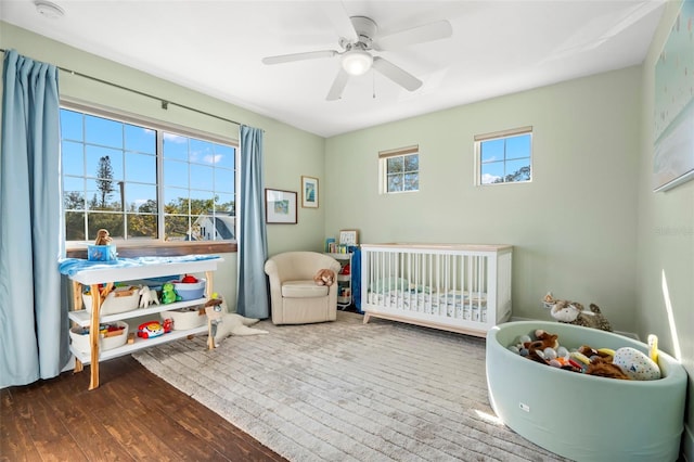 bedroom featuring dark hardwood / wood-style flooring, a crib, and ceiling fan