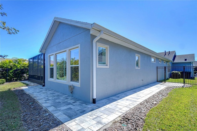 view of side of home featuring a yard, a patio, and glass enclosure