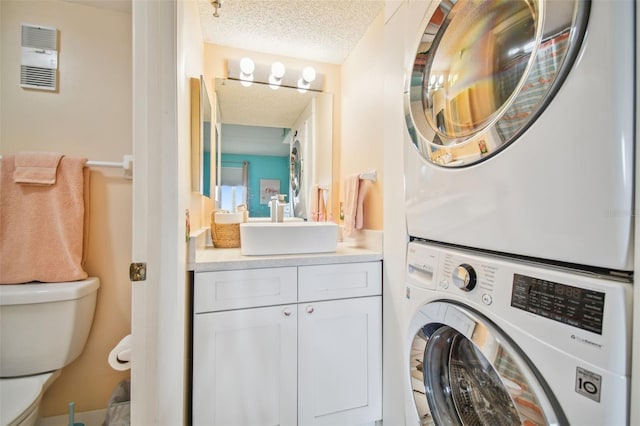 clothes washing area with sink, stacked washer and clothes dryer, and a textured ceiling