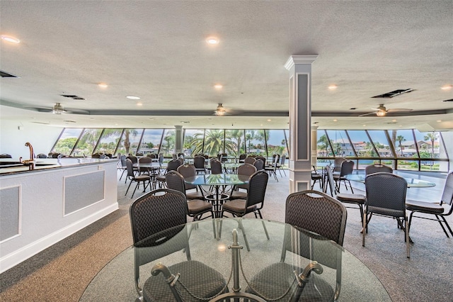 carpeted dining area featuring ceiling fan, sink, a textured ceiling, and ornate columns