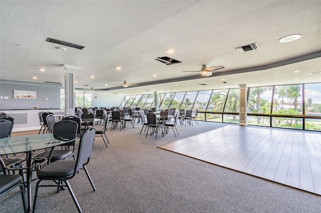 unfurnished dining area featuring ceiling fan, carpet flooring, a textured ceiling, and ornate columns