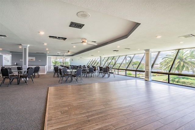 dining area featuring light hardwood / wood-style flooring, expansive windows, a textured ceiling, and ornate columns