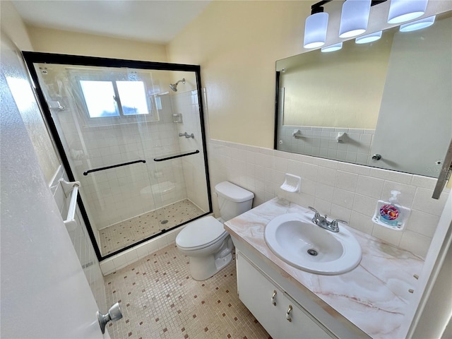 bathroom with toilet, a shower with shower door, tile walls, vanity, and tile patterned flooring