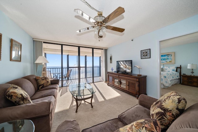 living room featuring expansive windows, light colored carpet, ceiling fan, and a textured ceiling