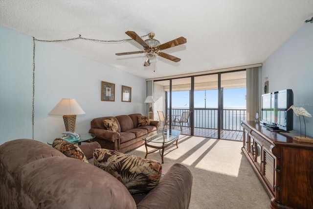 living room with ceiling fan, a wall of windows, and light colored carpet