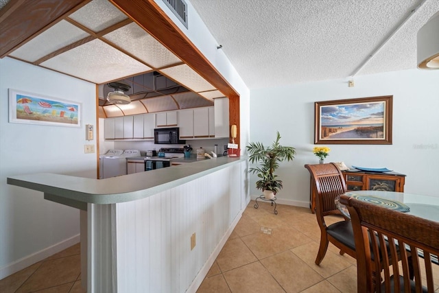 kitchen featuring a textured ceiling, light tile patterned floors, range with electric stovetop, washer and clothes dryer, and white cabinets