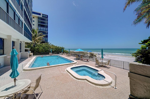 view of swimming pool with a water view, a beach view, a hot tub, and a patio