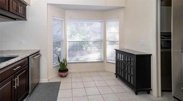 kitchen with light stone counters, stainless steel dishwasher, dark brown cabinets, and light tile patterned floors