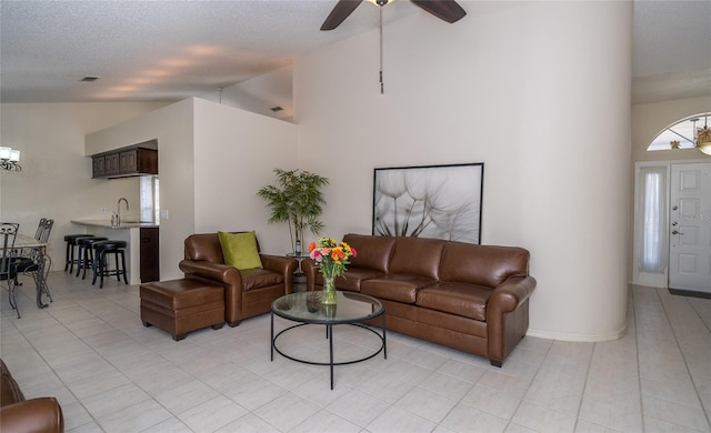 tiled living room featuring sink, ceiling fan with notable chandelier, high vaulted ceiling, and a textured ceiling