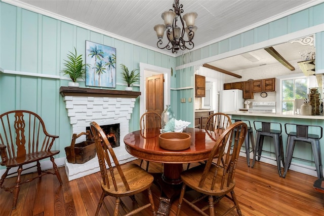 dining area featuring wood-type flooring, a stone fireplace, crown molding, and a chandelier