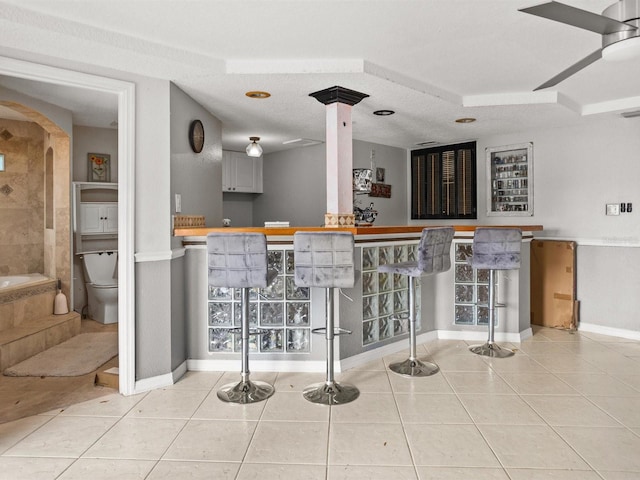 bar with bar area, a textured ceiling, baseboards, and light tile patterned floors