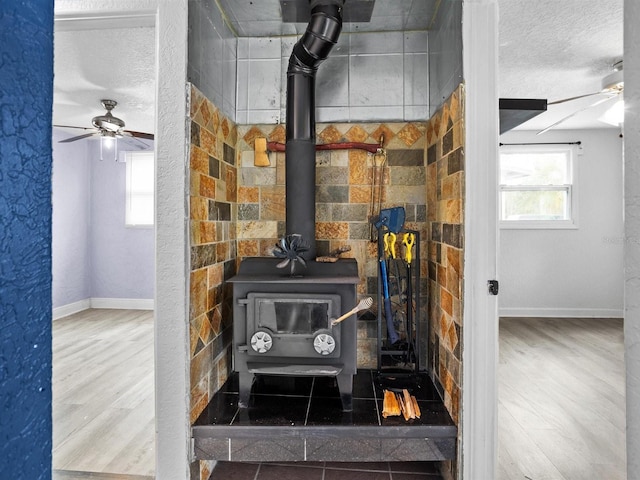 details featuring a ceiling fan, a wood stove, a textured ceiling, wood finished floors, and baseboards