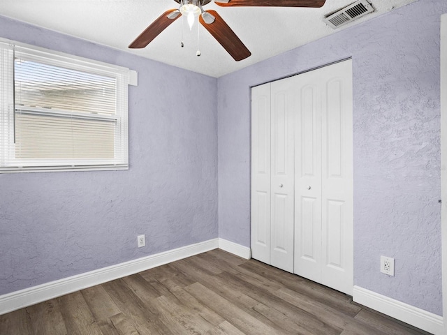 unfurnished bedroom featuring a textured wall, wood finished floors, visible vents, and baseboards