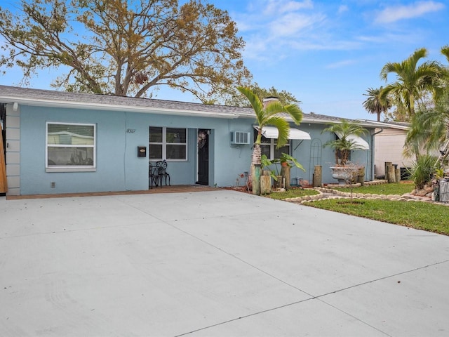 ranch-style house with a wall mounted AC, a front yard, and stucco siding