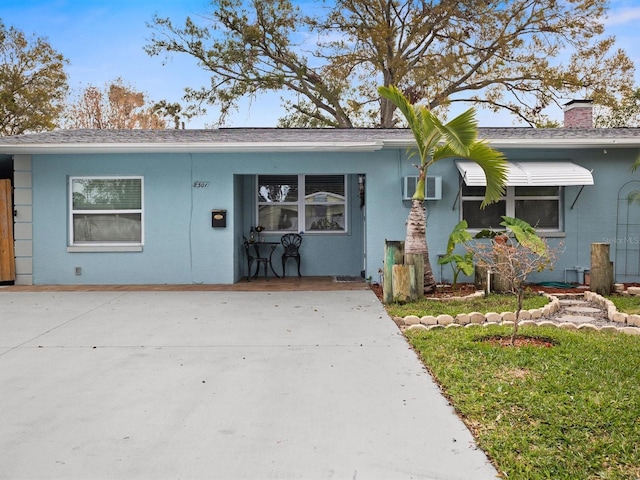 single story home featuring an AC wall unit, a chimney, a front lawn, and stucco siding