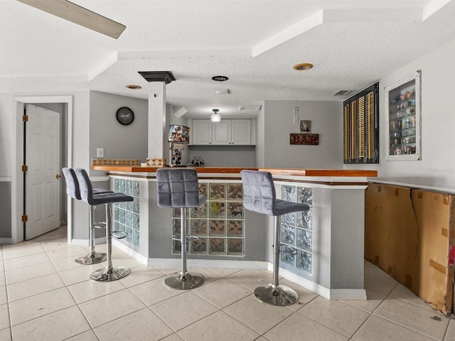 bar featuring light tile patterned floors, a bar, a textured ceiling, and visible vents