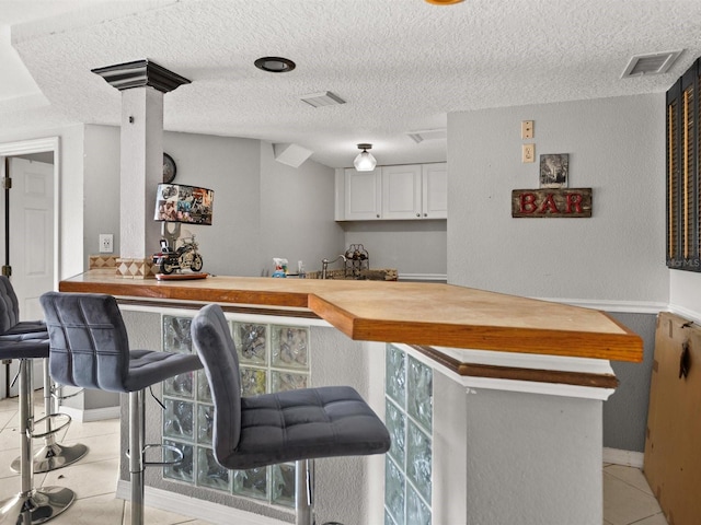 bar featuring a textured ceiling, a dry bar, light tile patterned floors, and visible vents