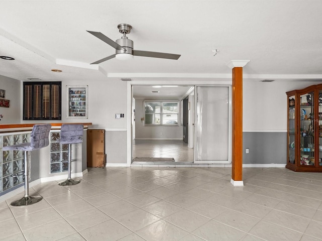 living room with light tile patterned flooring, visible vents, a ceiling fan, baseboards, and a bar