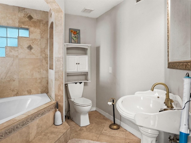 bathroom featuring visible vents, toilet, tiled tub, baseboards, and tile patterned floors
