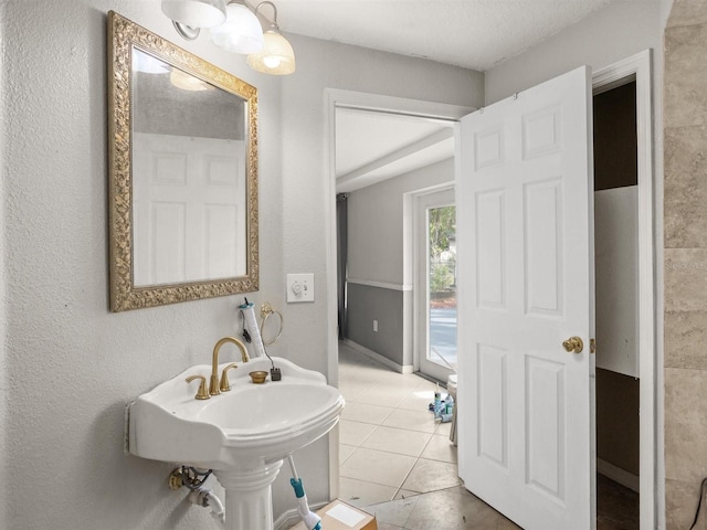 bathroom featuring a textured ceiling, a textured wall, a sink, and tile patterned floors
