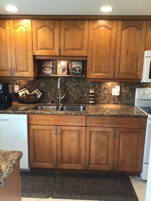 kitchen featuring tasteful backsplash, sink, dark stone countertops, dark tile patterned floors, and white appliances