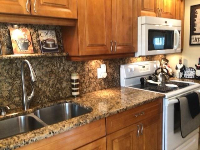 kitchen with tasteful backsplash, sink, white appliances, and stone counters