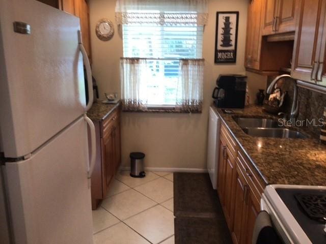 kitchen with light tile patterned flooring, white appliances, dark stone counters, and sink