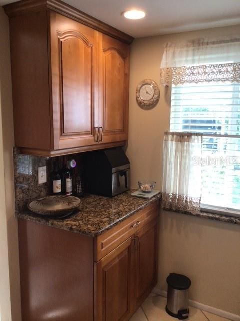 kitchen featuring light tile patterned flooring, plenty of natural light, decorative backsplash, and dark stone counters