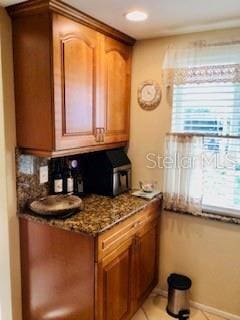 kitchen featuring stone counters, baseboards, brown cabinets, and light tile patterned floors