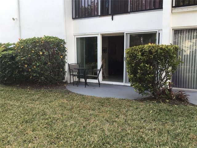 exterior space featuring a patio area, a balcony, a lawn, and stucco siding