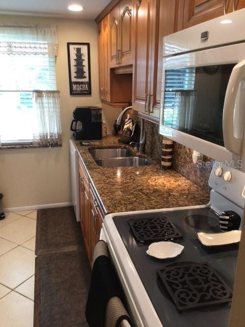 kitchen featuring white appliances, brown cabinetry, baseboards, light tile patterned flooring, and a sink